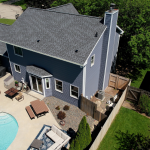 An aerial view of the back of a two-story blue house with an asphalt shingle roof and white windows