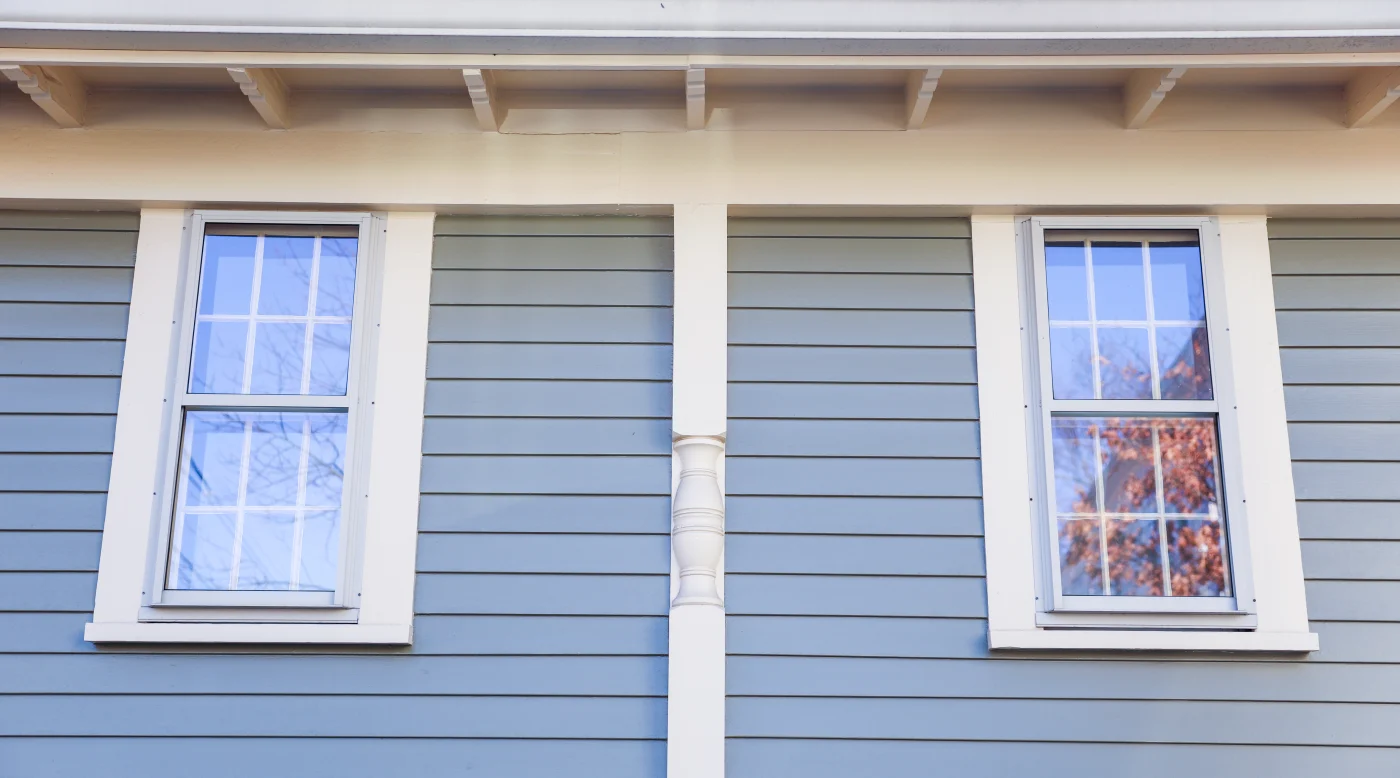 A close-up view of blue siding, white trim, and two white windows.