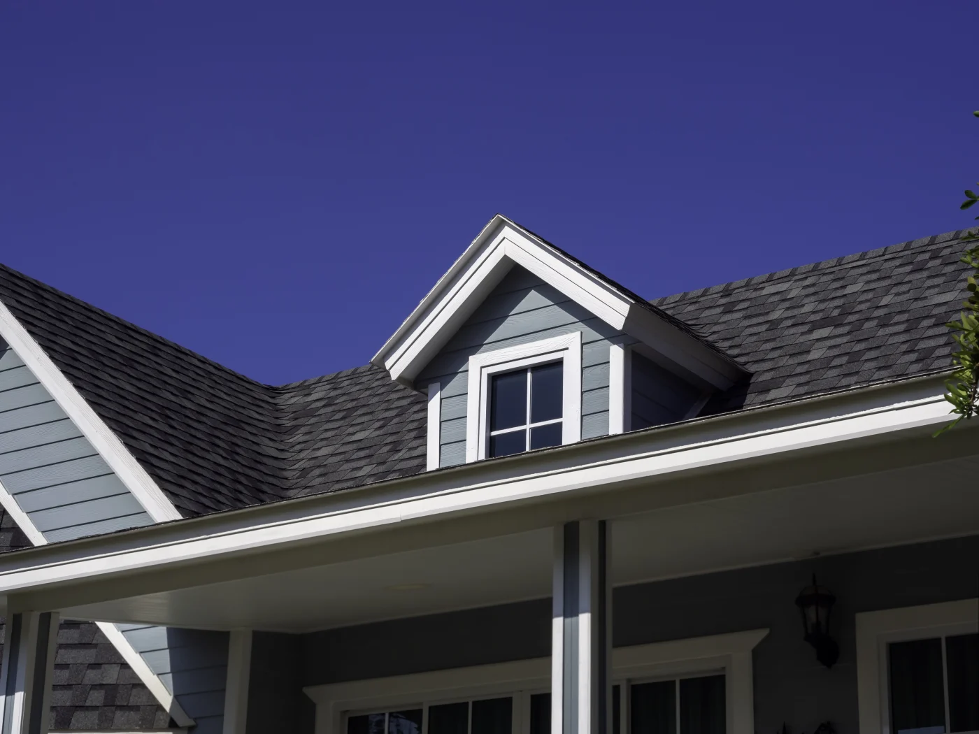 A close-up view of a gray house, white windows, and an asphalt shingle roof.