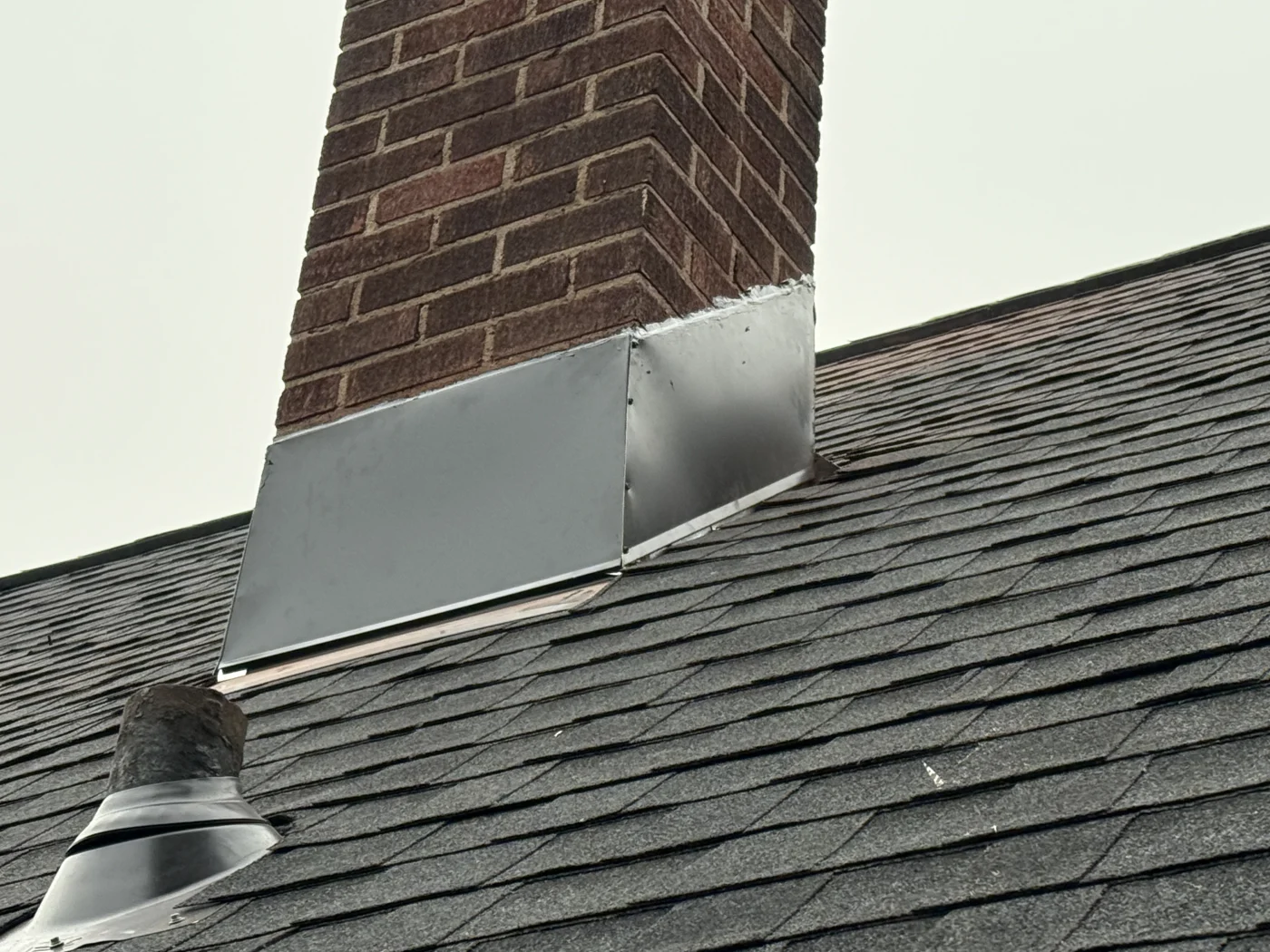Quality Roof Repair Kimberly Wi Wisconsin Exteriors A close-up view of an asphalt shingle roof with a brick chimney and metal flashing