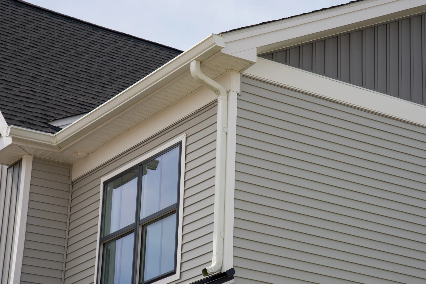 A close-up view of the corner of a gray house with brown windows.