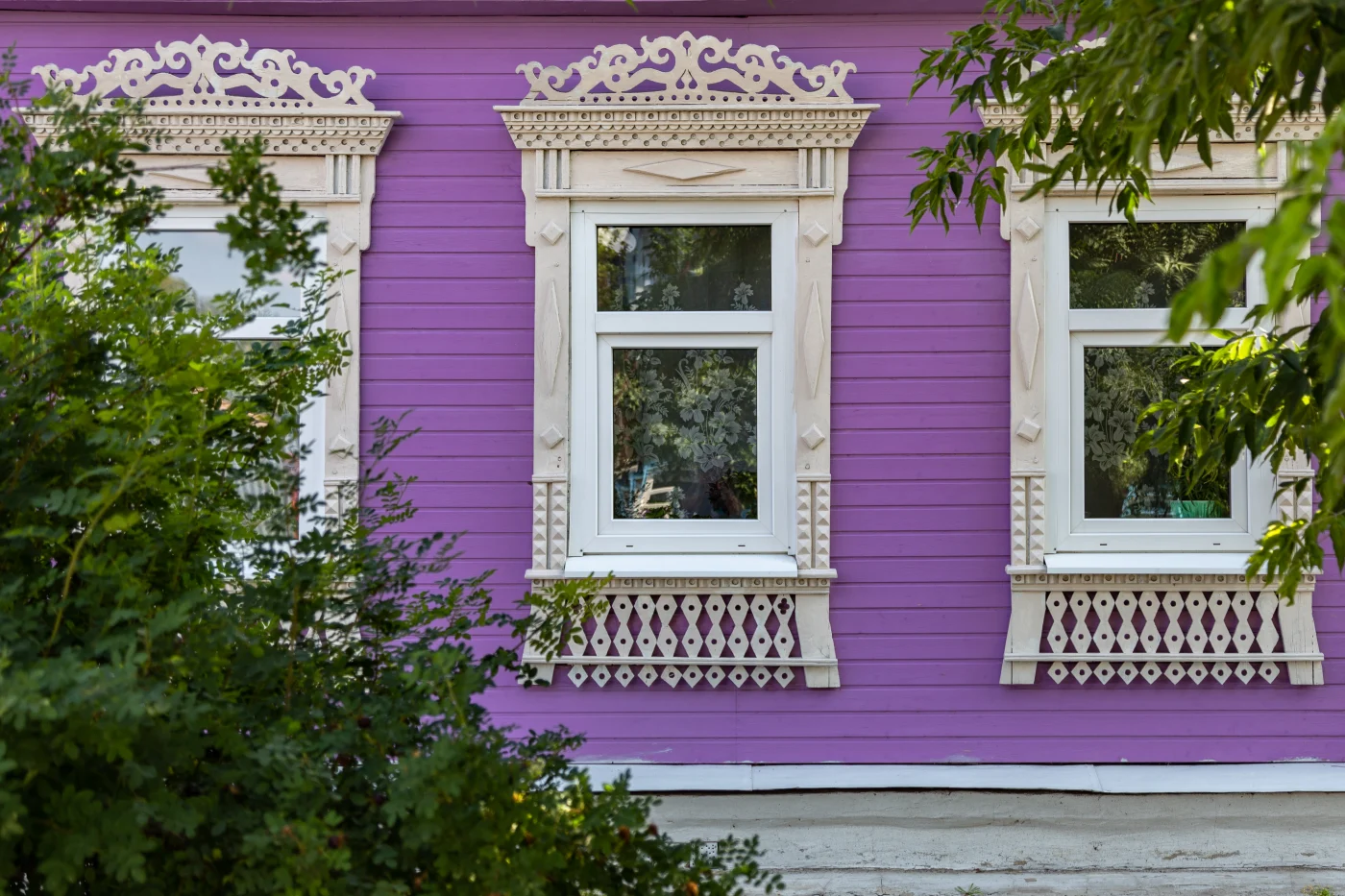 Three white windows with intricate tan frames on a purple house.