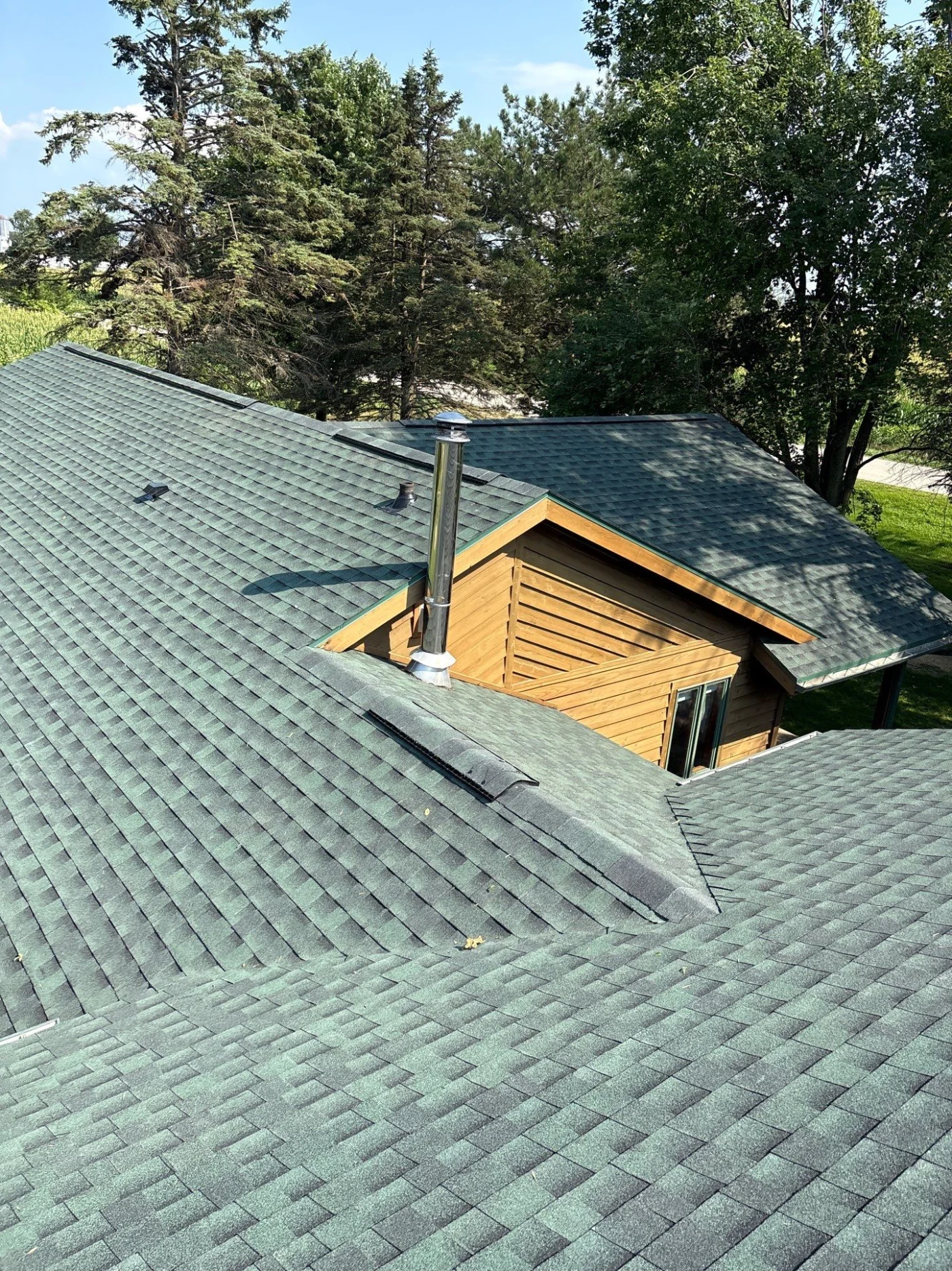 Wonderful Roof Inspection Kimberly Wi Wisconsin Exteriors A photo taken from on top of a multi-section roof, showing large sections of the surface. It’s covered in gray shingles, and the exterior of the home is covered in brown, woodgrain siding.