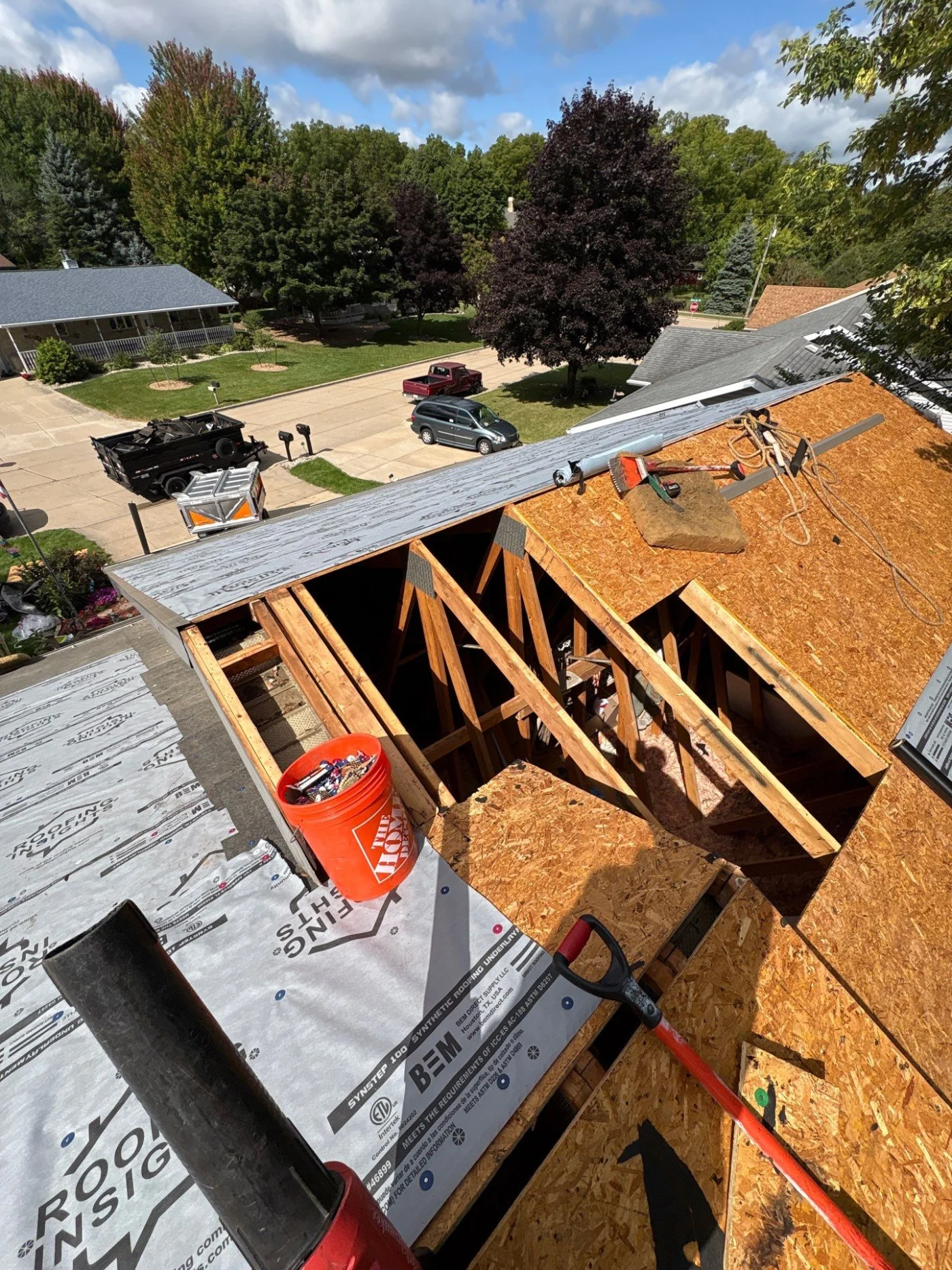 Worthy Roof Replacement Menasha Wi Wisconsin Exteriors A roof in the process of being rebuilt. Part of it is exposed down to the wooden base, another part has exposed beams, and the rest is covered in white protective underlayment. There are various tools and supplies visible on different sections of the roof.